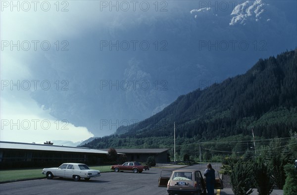 USA, Washington State, Mount St Helens Volcanic eruption 1980 at 8.40am. View from car park with a person standing outside a car looking towards forest covered mountain with billowing ash rising