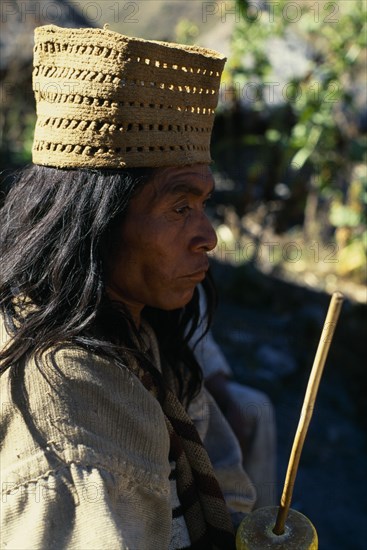 COLOMBIA, Sierra Nevada de Santa Marta, Valley of Surlivaka, Parque Nacional. Kogi mama/priest Juan Vacuna wearing a woven fique/cactus fibre hat  holding a lime-encrusted poporo/gourd  with a palito/stick used to transfer lime powder out of the gourd and into a wad of coca leaves held in cheek. Lime acts as catalyst releasing very small amount of cocaine from coca leaves. Mama Juan wears traditional woven cotton manta/cloak.