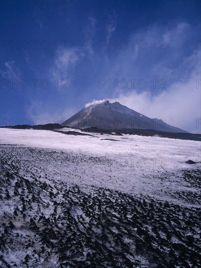 ITALY, Sicily, Mount Etna, The summit cone seen from across a lava field covered with snow.