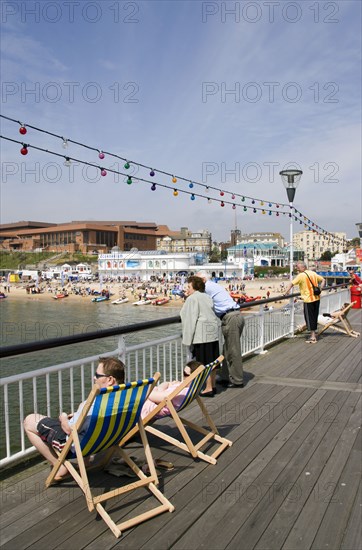 ENGLAND, Dorset, Bournemouth, The West Beach from The Pier with the BICC Bournemouth International Conference Centre and Oceanarium in the distance. Tourists on deckchairs on the pier