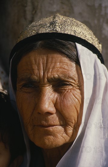 CHINA, Xinjiang, Kashgar, Portrait of an old woman at the Sunday market. Wearing a white head scarf and gold with black trim hat.