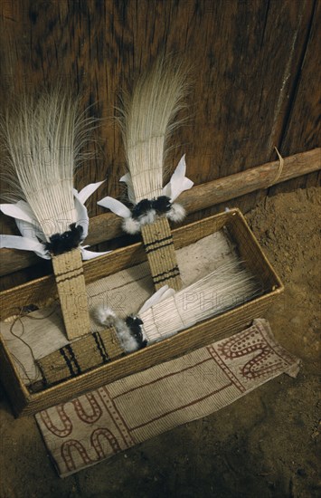 COLOMBIA, Vaupes Region, Tukano Tribe, "Sacred box of ceremonial feather head-dresses, ritual adornments, hung from “maloca” longhouse roof and brought down only for festivals /dances. Royal crane tail feather headdress, dyed bark-cloth apron in foreground"