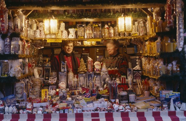 GERMANY, Bayern, Nuremberg, "Women vendors in decorated stall in Christmas market selling glassware, candles and Christmas decorations."