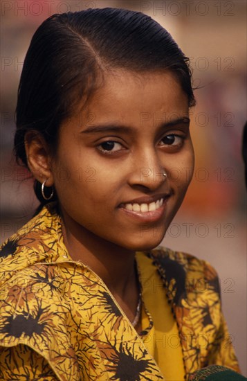 INDIA, Uttar Pradesh, Varanasi, Head and shoulders portrait of young girl on the ghats wearing a yellow shirt with a nose stud and earrings.