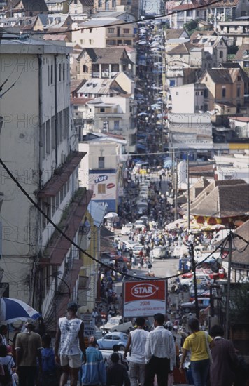 MADAGASCAR, Antananarivo, Downtown area. People walking down towards a busy road running between buildings and shopfronts filled with people and cars