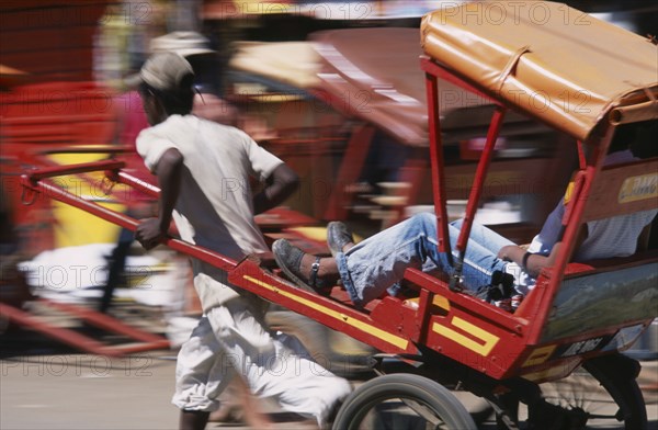 MADAGASCAR, Antsirabe, Rickshaw driver traveling along road in motion blur