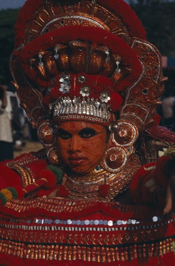 INDIA, Kerala, Thrissur, "Theyyam dancer in a red costume and painted face, at The Great Elephant March festival."