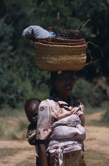 MADAGASCAR, People, Women , Near Ambositra. Portrait of a woman carrying a baby in a sling on her back and wicker baskets on her head