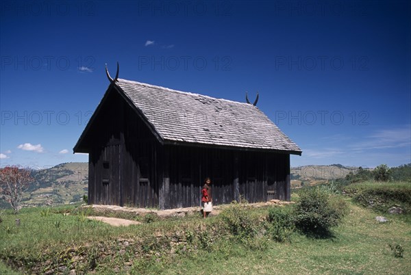 MADAGASCAR, Architecture, Near Ambositra. Royal wooden hut used by former Malagasy King with a woman standing outside exterior