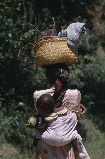 MADAGASCAR, People, Women, Near Ambositra. Portrait of a woman carrying a baby in a sling on her back and wicker baskets on her head