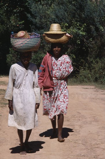 MADAGASCAR, People, Women, Near Ambositra. Two barefooted women walking up a dirt track carrying wicker baskets on their heads