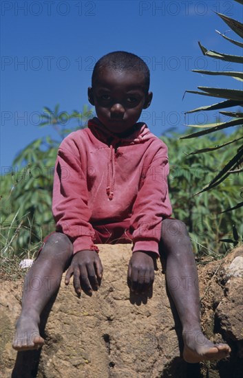 MADAGASCAR, People, Children, Near Ambositra. Portrait of a young child wearing a red hooded top sitting on a wall