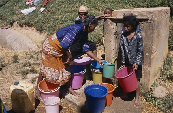 MADAGASCAR, Ambositra, A woman with children collecting water from a nearby public supply point with colourful buckets
