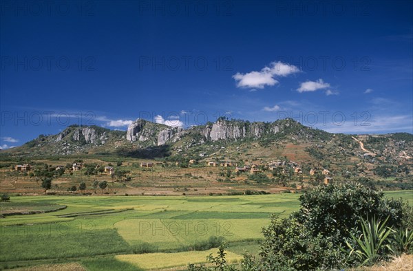MADAGASCAR, Landscape, Road to Ambalavao.  View across green paddy fields towards a village of thatched huts set into hillside