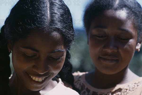 MADAGASCAR, People, Women, Road to Ranomanfana. Portrait of two young women smiling with their eyes looking down one girl with plaited pig tails