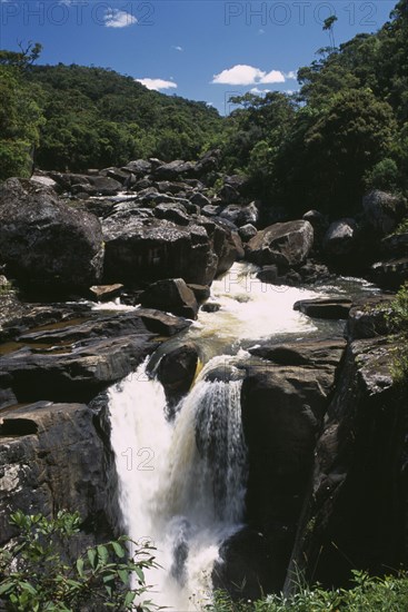 MADAGASCAR, Ranomanfana National Park, Waterfalls cascading over rocks surrounded by lush green tropical rainforest
