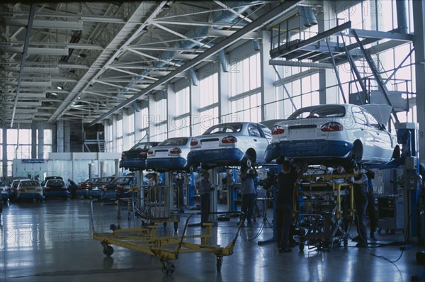 UKRAINE, Zaporozhye, Cars raised off the ground with staff working underneath in a production factory.