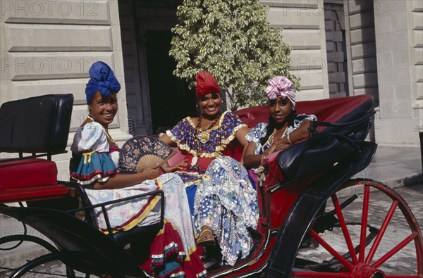 CUBA, Havana, Three woman tourist dancers dressed in costume sat in a horse carriage