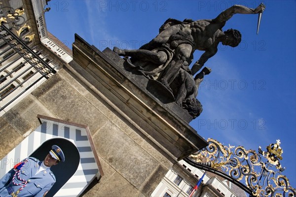 CZECH REPUBLIC, Bohemia, Prague, Soldier standing guard at a sentry box below an 18th Century statue of fighting giants by Ignaz Platzer at the entrance to Prague Castle in Hradcany