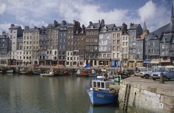 FRANCE, Normandy, Calvados, "Honfleur harbour with fishing boats moored against stone quay overlooked by tall, narrow houses."