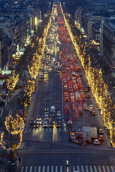 FRANCE, Ile de France, Paris, Les Champs Elysees at night with illuminated shop fronts and traffic lights.