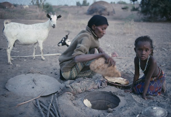 ETHIOPIA, North East, Afar tribeswoman baking bread in ground with child sitting beside her.