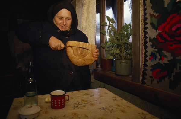ROMANIA, Maramuresh, Elderly widow cutting bread.