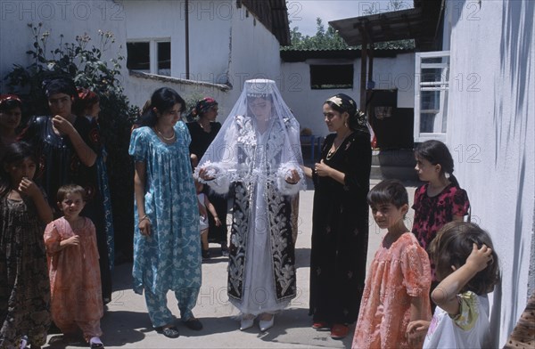 TAJIKISTAN, Wedding, "The bride wearing a veil and highly decorated jacket, surrounded by guests at a village wedding."