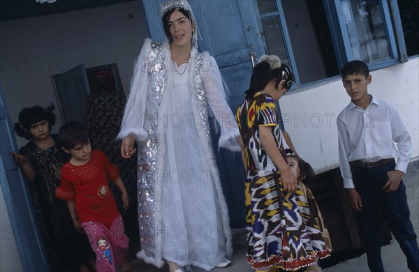 TAJIKISTAN, Wedding, "The bride wearing a white dress and silver jacket, with children around her at a village wedding."