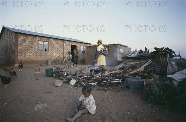 SOUTH AFRICA, Orange Free State, Mother and children outside their home with chickens and cooking fire.  Young child playing in the dirt in the foreground.
