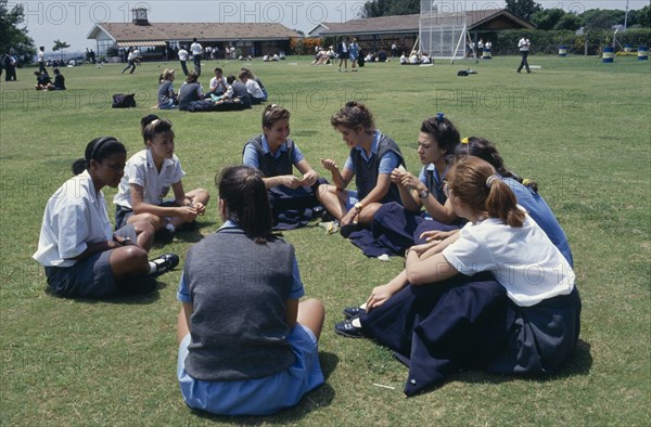 SOUTH AFRICA, Guateng, Johannesburg, Mixed race group of schoolgirls sitting on playing fields during break.