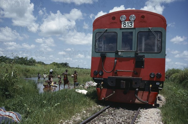 CONGO, Transport, Train passing people and children doing laundry in river in rural area.