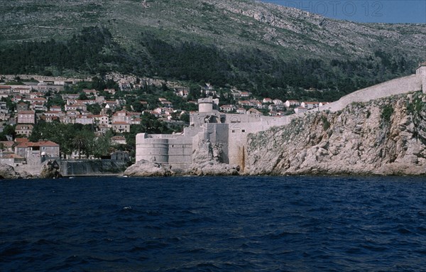 CROATIA, Dalmatia, Dubrovnik, View across water towards the Old City fortifications along the coastline and houses built into the hillside.