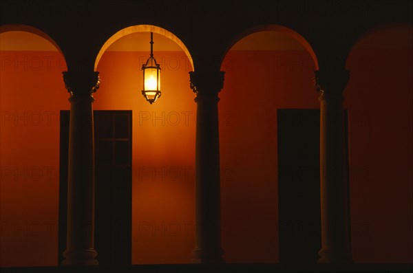 PUERTO RICO, San Juan, Exterior of building at night with pillars and arches and a single light illuminating an orange wall