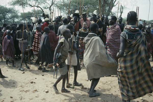 UGANDA, Karamoja District, Karamojong warriors at Akuidakin ceremony to bless cattle and ask for rain.  Young girl dancing in centre is painted with Giraffe clan markings.