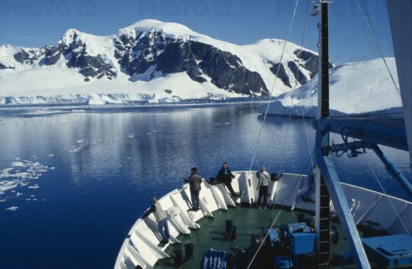 ANTARCTICA, Peninsula Region, View of the front section of a ship with people standing looking over edge surrounded by snow covered mountains