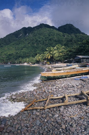 DOMINICA, Windward Islands, Soufriere Bay, Scotts Head fishing village. View across stoney beach lined with wooden fishing boats and huts towards palm trees and tree covered hillside