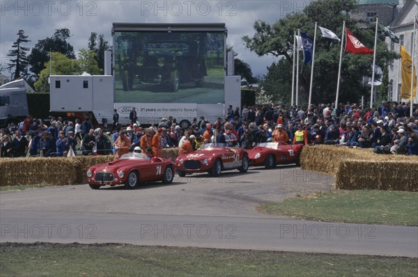 ENGLAND, West Sussex, Goodwood, Festival of Speed. Three red Ferraris 2 litre built in 1950 4.1 litre 1953 and 4.1litre 1957. Crowds of spectators gathered around circuit