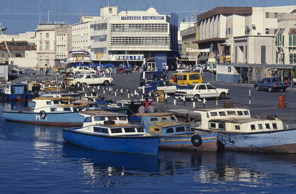 BARBADOS, Bridgetown, Moored painted boats on the Careenage with busy shopping district beyond.