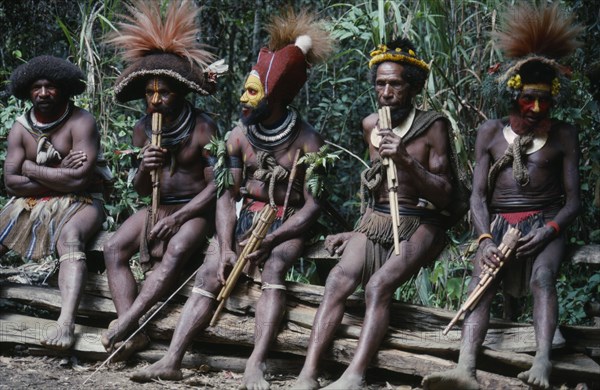PACIFIC ISLANDS, Melanesia, Papua New Guinea, Southern Highlands. Huli tribe men sat together playing wood instruments at Bachelor Boys centre