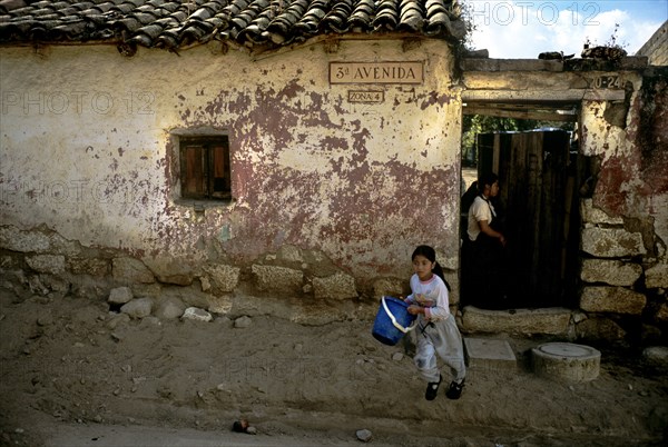 GUATEMALA, Quetzatenango, Xela, "Water shortages in the outskirts of the town of Xela. Eenvironmental destruction, implicit in open pit mining, continues to damage the ecosystems in Guatemala. Forests, water sources, flora and fauna are all heavily effected. Cyanide and heavy metal contamination of several water sources in the area has been confirmed. There are communities that have drunk water with high concentrations of arsenic, mercury and lead for years, while other communities must travel to another municipality in order to obtain enough clean water for domestic use. Efforts are slowly being made to transport usable water to the regions most effected, but as always, the deliveries are erratic and unreliable. These local indigenous kids have waited for hours for a delivery of 'drinkable' water. The youngest one runs from her house across the dusty road with a large blue plastic bucket, ready to be filled to the brim. Her older sister watches on in the background, staying by the woo...