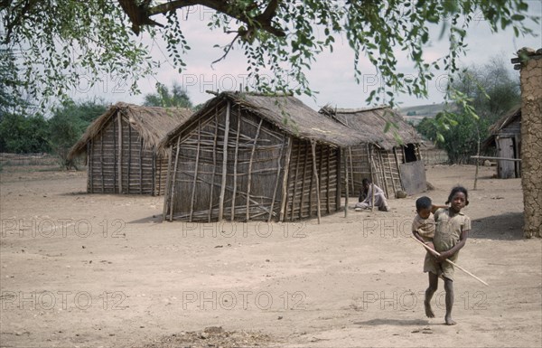 MADAGASCAR, Tulear, Village homes with a young girl carrying a younger child in the foreground