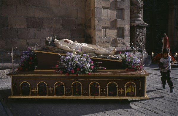 MEXICO, San Luis, Potosi, Crucified Christ lying vertically in a Easter Procession with a boy running along pavement.