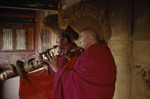 CHINA, Qinghai Province, Quezhang Lamasery, Tibetan Yellow Hat Buddhists playing long trumpet horns know as Dung Chen.