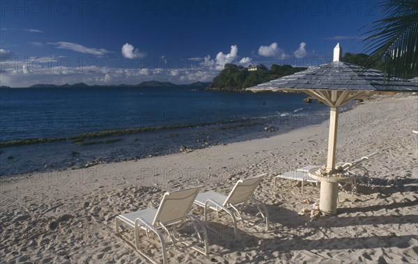 GRENADINES, Mustique, Endeavour Bay. Empty sun loungers on sandy beach with Bequia Island seen from across the sea in the distance