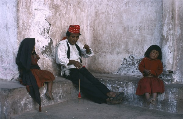 PERU, Puno, Lake Titicaca, Taquile man spinning wool with his two children sitting either side of him.