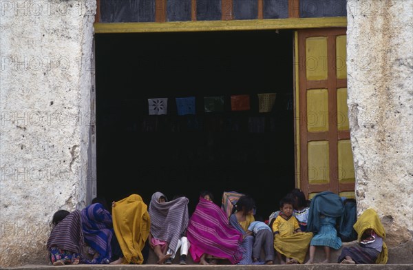 MEXICO, Chiapas, Children sitting in doorway of building wrapped in colourful blankets as protection against the cold.