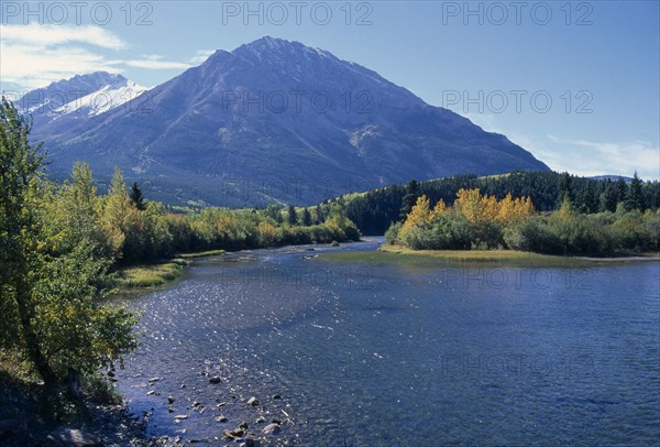 CANADA, Alberta, Landscape near Crowsnest Pass with river flanked by trees in fall colours and snow topped mountains beyond.