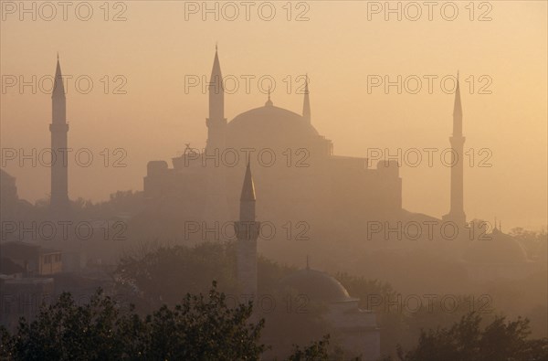 TURKEY, Istanbul, "Dome and minarets of Haghia Sophia silhouetted against hazy, pale orange sky amongst rooftops of the Sultanahmet.  Former mosque now museum."