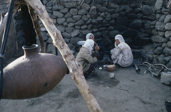 TURKEY, East, Nemrut, Women sitting on ground beside suspended vessel used to churn milk.